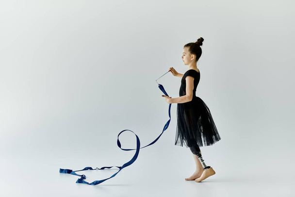 Młoda dziewczyna z protezą nogi wykonuje pełen wdzięku taniec wstążki w studiu. - Zdjęcie, obraz