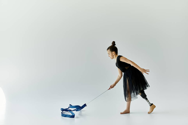 Ein junges Mädchen mit Beinprothese führt in einem weißen Studio eine anmutige Schleifenroutine durch. - Foto, Bild