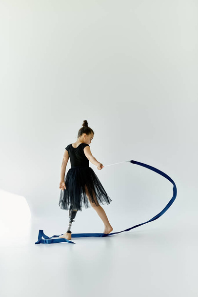 Молодая девушка с протезной ногой исполняет гимнастический номер с голубой лентой.. - Фото, изображение