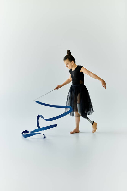 Una giovane ragazza con una gamba protesica esegue ginnastica con un nastro blu. - Foto, immagini