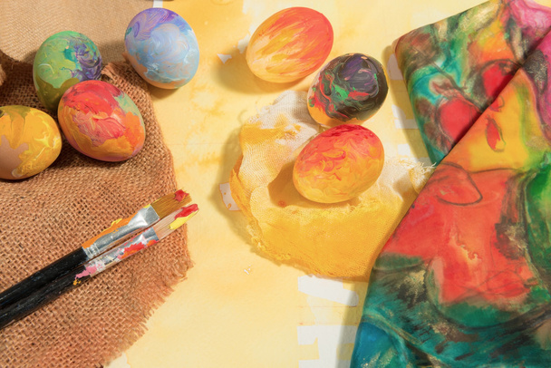 Huevos coloridos de Pascua con dos pinceles de pintor, una paleta de madera y un paño pintado a mano
. - Foto, Imagen