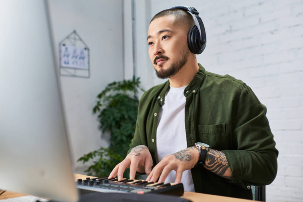 An Asian man with headphones plays a keyboard in his studio. - Photo, Image