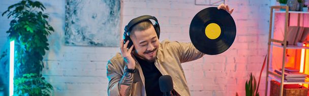 A handsome Asian man podcasting in a brightly lit studio, holding a vinyl record. - Photo, Image