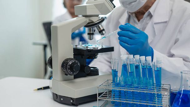研究室で働く2人のアジア人科学者は,生物学と化学を研究している科学者です. カップルは眼鏡をかけ,顕微鏡,医療コンセプトを調べる - 写真・画像