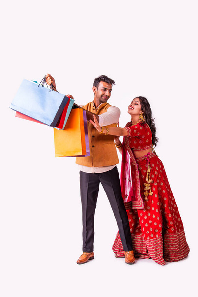India pareja asiática con bolsas de compras en ropa étnica, de pie aislado sobre fondo blanco. Diwali o venta de festivales - Foto, Imagen