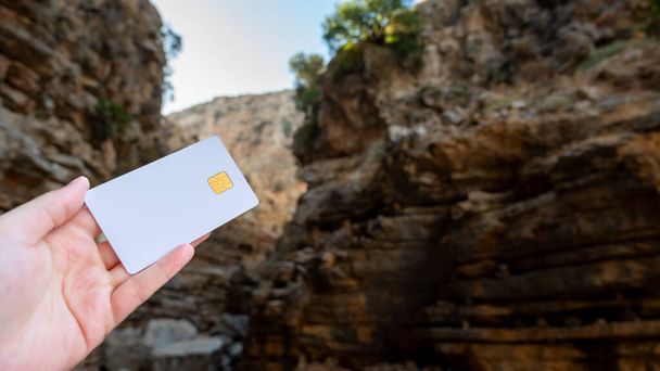 Contra uma paisagem pitoresca, uma pessoa está segurando um cartão de crédito com uma montanha no fundo. Foto de alta qualidade - Foto, Imagem