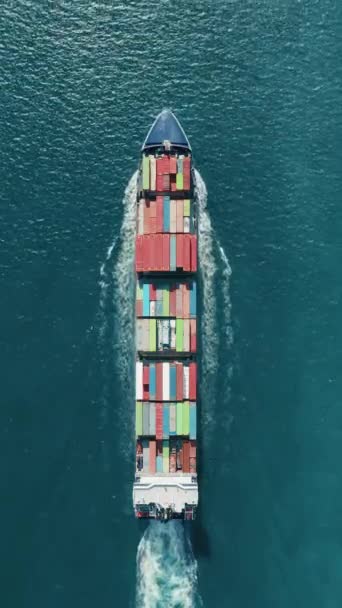 Pystysuora näyttö: Antenninäköala vangitsee suuren rahtialuksen, jossa on värikkäitä kontteja, jotka purjehtivat valtameren läpi ja esittelevät logistiikka- ja merenkulkualaa tavaroiden kuljettamisessa maailmanlaajuisesti - Materiaali, video
