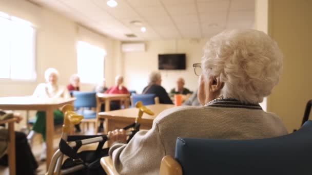 Nagyítás lassított felvételen idős emberek ülnek asztaloknál világos szobában az idősek otthonában nappal - Felvétel, videó