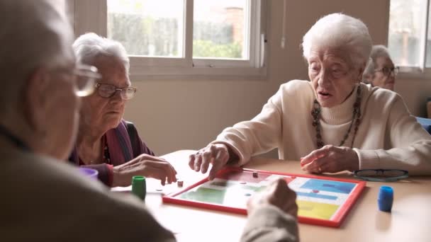 Αργή κίνηση των ηλικιωμένων γκριζομάλλης γυναίκες και άνδρες συνταξιούχοι κάθονται γύρω από το τραπέζι και παίζουν επιτραπέζιο παιχνίδι κατά τη διάρκεια του ελεύθερου χρόνου - Πλάνα, βίντεο