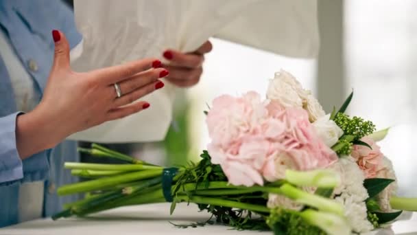 egy virágüzletben egy virágárus fehér papírba csomagol egy kész, finom csokrot. - Felvétel, videó