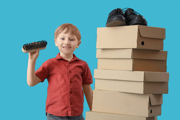 Petit garçon mignon avec brosse de nettoyage et boîtes à chaussures sur fond bleu - Photo, image