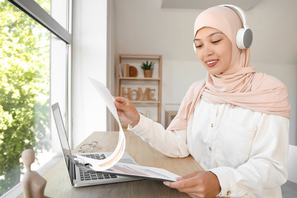 Joven mujer de negocios musulmana en auriculares con portapapeles trabajando en casa - Foto, imagen