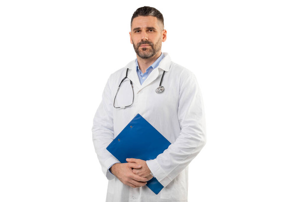 Um médico homem está de pé com prancheta em suas mãos, enquanto vestindo um estetoscópio em torno de seu pescoço, indicando prontidão e profissionalismo em um ambiente médico. - Foto, Imagem