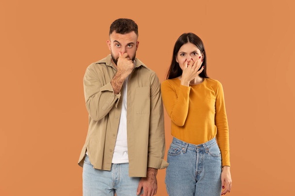 Egy férfi és egy nő narancssárga háttér előtt állnak, kezükkel befogják az orrukat. Mindkettő alkalmi ruhában van. - Fotó, kép
