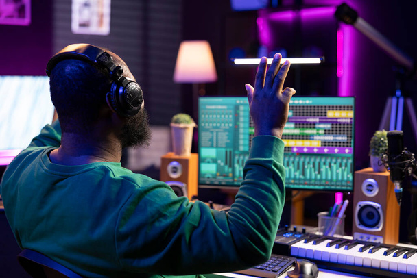 Técnico de audio experto afroamericano cuenta atrás antes de grabar una canción, haciendo una sesión en su estudio en casa. Productor que opera en consola de mezcla y software digital, equipo estéreo. - Foto, imagen