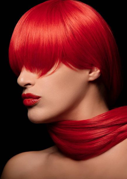 Mooi model met levendige rood geverfd haar en rode lippen, presentatie van elegantie en stijl, geïsoleerd op een zwarte achtergrond. Perfect voor schoonheid, kapsel en mode thema 's. - Foto, afbeelding