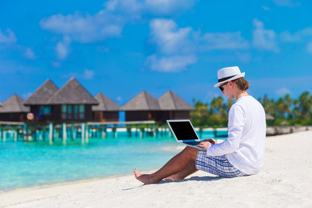 水上ヴィラの近くの熱帯のビーチでノート パソコンを持つ若者 - 写真・画像