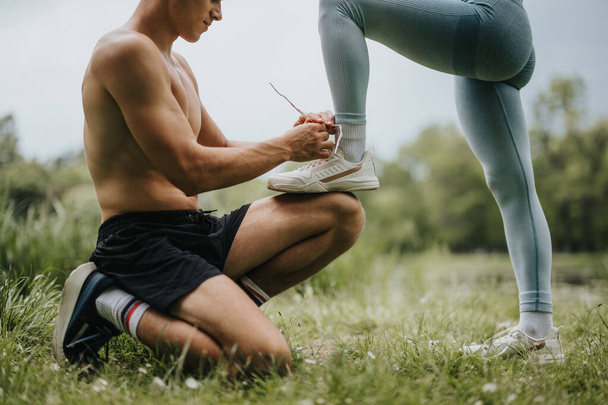 Man kneeling and tying shoelaces for his female partner during a workout in the park, promoting fitness and outdoor exercise. - Foto, Imagem