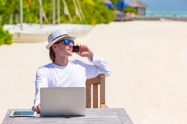 Young man with tablet computer and cell phone on tropical beach - Photo, image