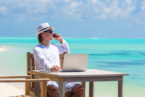 Nuori mies tabletti tietokone ja matkapuhelin trooppisella rannalla
 - Valokuva, kuva