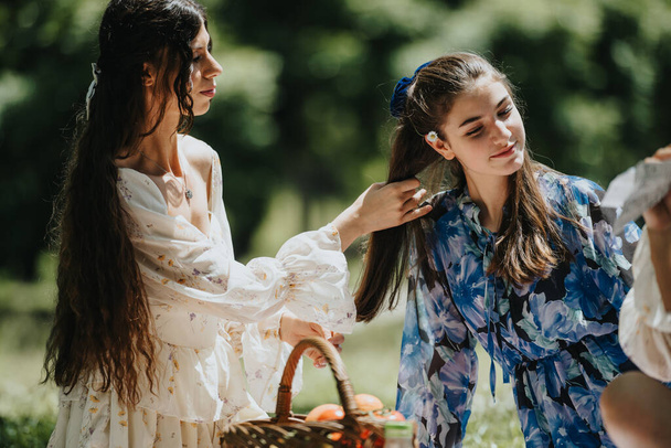 Obraz uwieczniający dwie młode kobiety, być może przyjaciółki lub siostry, urządzające piknik w bujnym parku w słoneczny dzień. - Zdjęcie, obraz