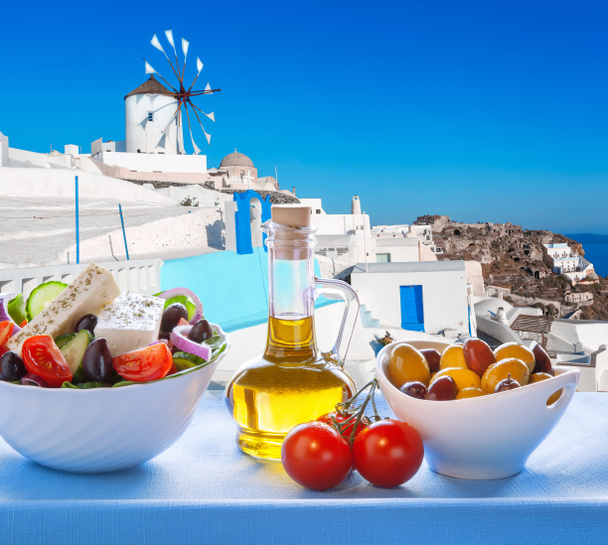 Greek salad against windmill in Oia village, Santorini island in Greece - Photo, Image
