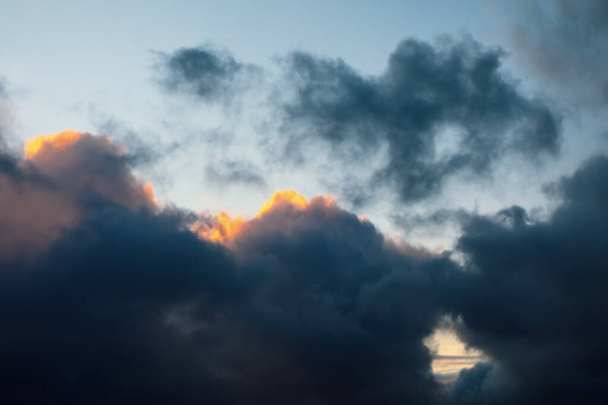 Donkere wolken tegen een zonsondergang achtergrond. sombere wolken contrasteren met de avondgloed - Foto, afbeelding