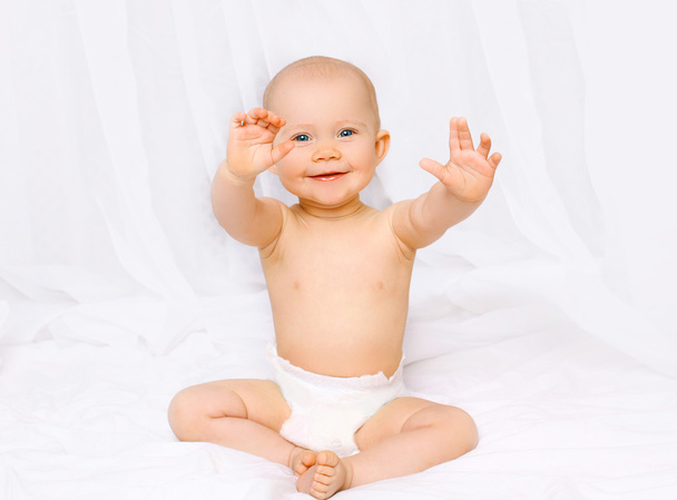 Active laughing baby sitting in diapers and having fun on the be - 写真・画像