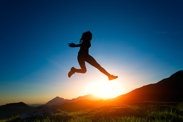 Chica salta durante una puesta de sol en las montañas
 - Foto, Imagen