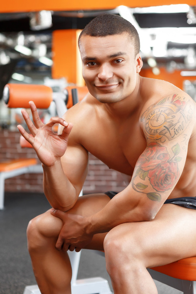 Muscular man sitting in gym and pointing ok - Foto, afbeelding