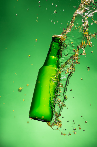 Bottle of beer with splash, on green background - Foto, afbeelding