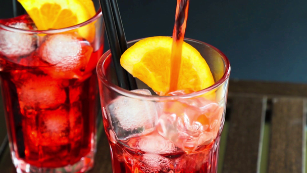 Barmann gießt Aperitif-Cocktail mit rotem Spritz und zwei Orangenscheiben und Eiswürfeln - Filmmaterial, Video