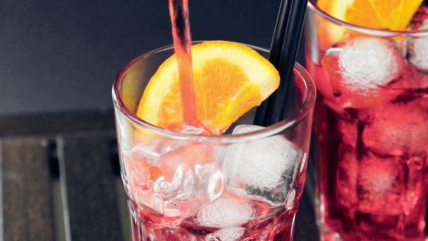 Barmann gießt Aperitif-Cocktail aus rotem Spritz mit zwei Orangenscheiben und Eiswürfeln auf Holztisch - Filmmaterial, Video