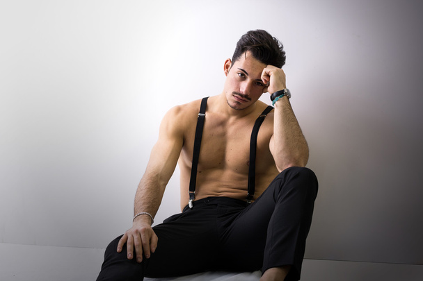 Shirtless athletic young man with suspenders sitting on floor - Photo, Image
