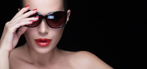Stylish woman wearing sunglasses on black background, showcasing red lips and nails. Isolated with copy space. - Photo, Image