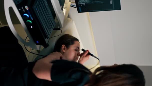 vídeo vertical em uma clínica de oftalmologia um jovem médico realiza um ultra-som do olho de uma jovem - Filmagem, Vídeo