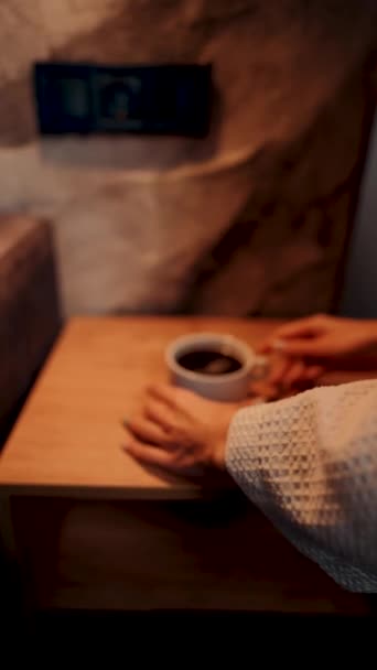 バスローブの若い女性がコーヒーを飲んで,山のホテルの窓を眺める. ホテルホリデーコンセプト。 バーティカルビデオ - 映像、動画
