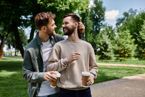 Una coppia gay barbuto gode di un appuntamento caffè in un parco verde lussureggiante, condividendo un momento tenero. - Foto, immagini