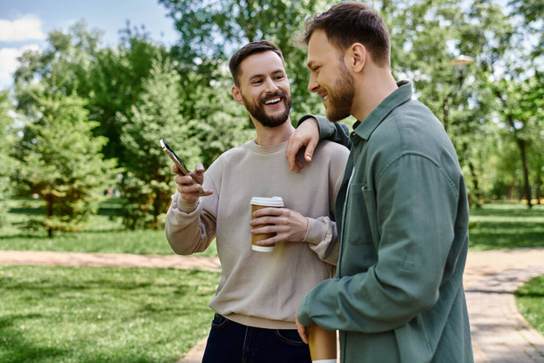 Δύο γενειοφόροι άνδρες σε casual ρούχα γελούν μαζί σε ένα πράσινο πάρκο, απολαμβάνοντας μια ηλιόλουστη μέρα. - Φωτογραφία, εικόνα