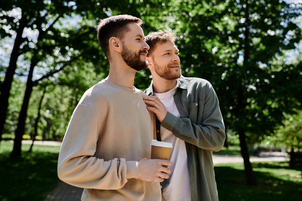 Una coppia gay con la barba si gode una pausa caffè in un parco verde, condividendo un momento di amore e intimità. - Foto, immagini