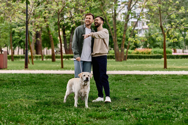 Una pareja gay barbuda con atuendo casual sonríe y disfruta de un día en el parque con su perro labrador. - Foto, Imagen