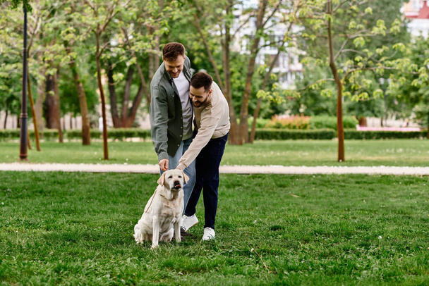 Egy szakállas meleg pár alkalmi ruhában minőségi időt tölt a labrador kutyájával egy zöld parkban egy napsütéses napon.. - Fotó, kép