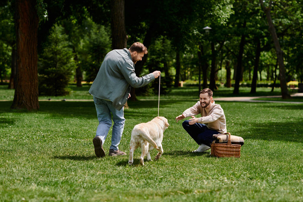 Una pareja gay barbuda con atuendo casual pasan tiempo juntos en un parque verde, jugando a buscar con su perro labrador. - Foto, imagen