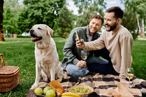 Una pareja gay barbuda disfruta de un picnic con su perro labrador en un parque verde en un día soleado. - Foto, imagen