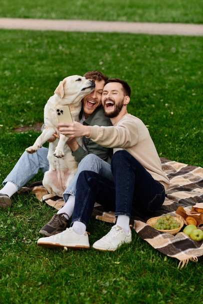 A bearded gay couple laughs as their labrador dog nuzzles them during a picnic in a green park. - Photo, Image