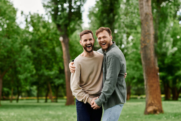 Ein bärtiges homosexuelles Paar umarmt sich fröhlich in einem üppig grünen Park, ihr Lachen hallt durch die Bäume.. - Foto, Bild