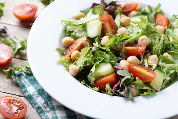 木のテーブルにトマト,レタスおよびキュウリが付いている健康なひよこ豆のサラダ - 写真・画像