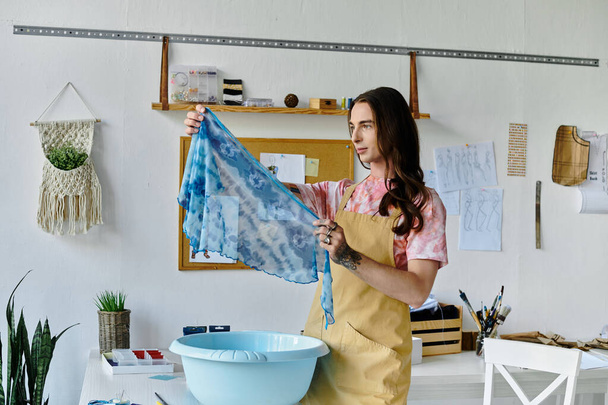 A young man examines a piece of tie-dyed fabric he is restoring in his clothing atelier, focusing on sustainability and giving new life to old items. - Photo, Image