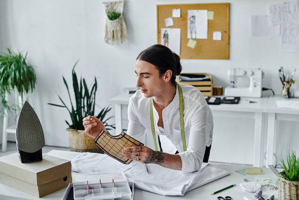 Un giovane uomo in camicia bianca esamina un modello di tessuto, mostrando la sua dedizione al restauro sostenibile della moda nel suo atelier. - Foto, immagini