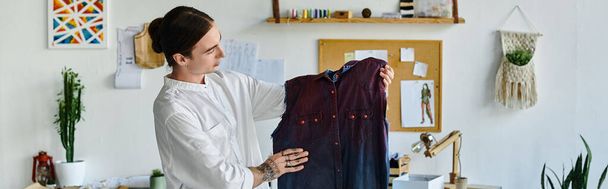 Młody mężczyzna, ubrany w białą koszulę, bada odnowioną odzież w pracowni renowacji odzieży DIY, podkreślając zrównoważone praktyki. - Zdjęcie, obraz
